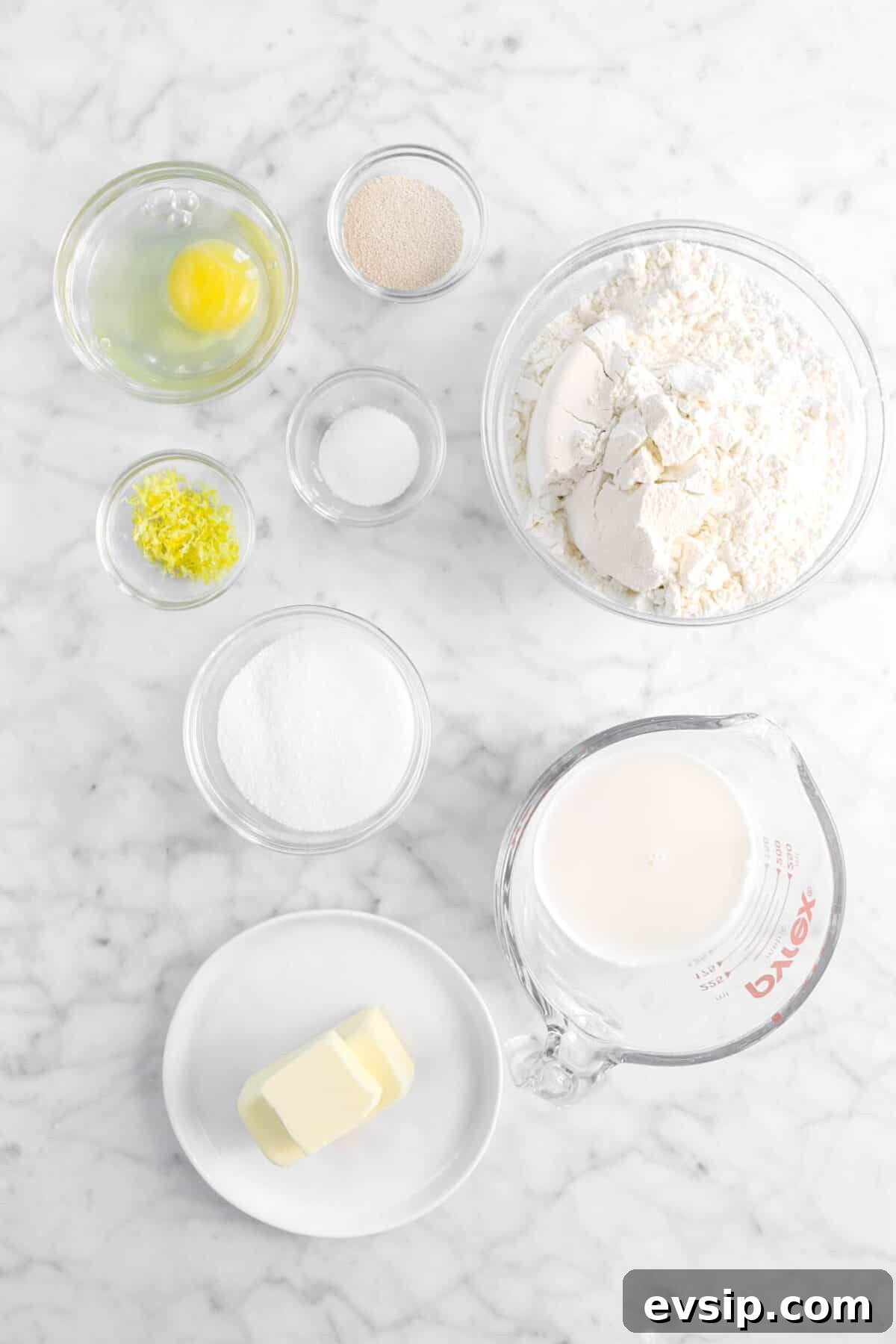 egg, yeast, flour, baking powder, lemon zest, sugar, milk, and butter on marble counter