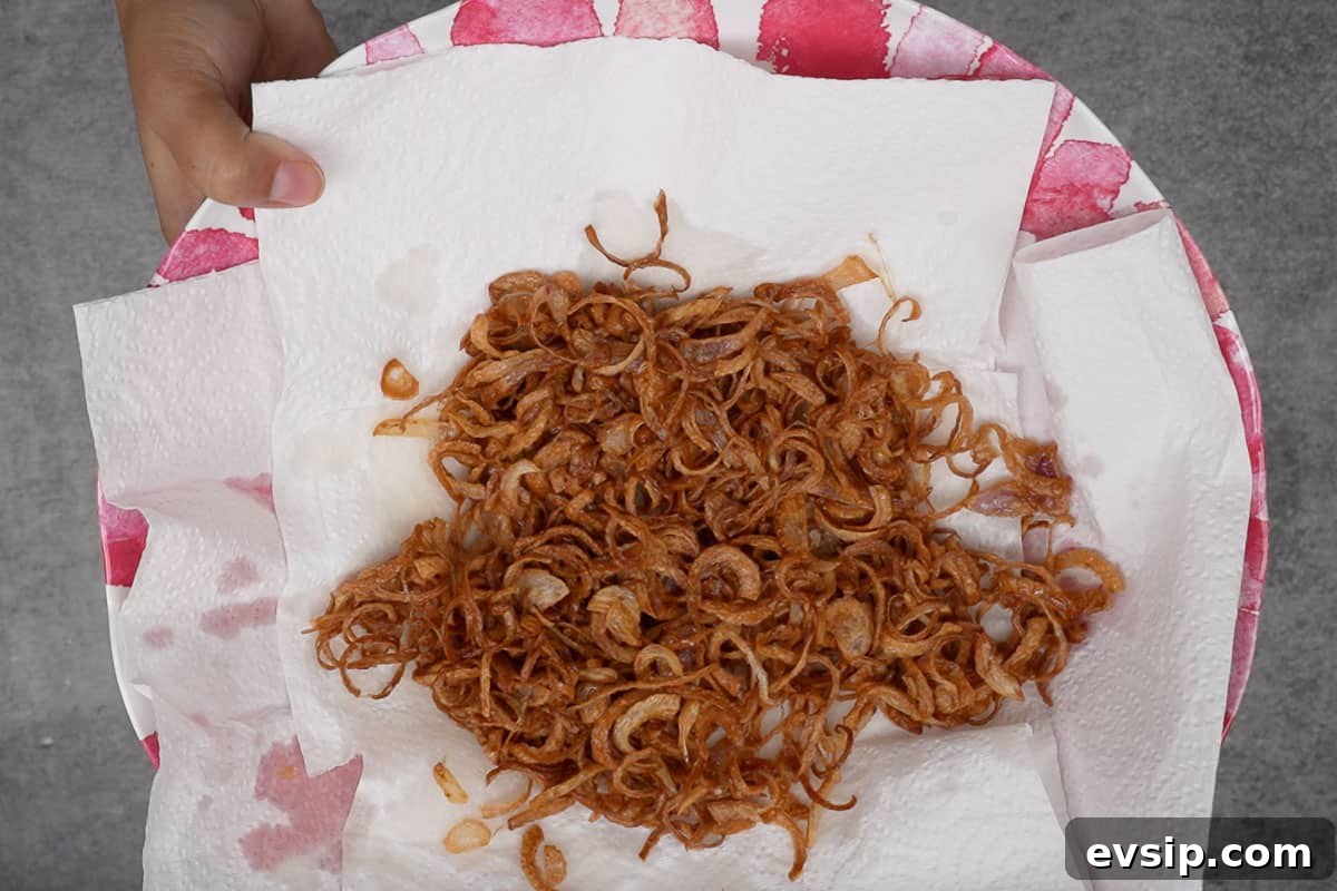 Ready crispy fried onions spread on a plate lined with paper towels.