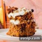 slice of two layer carrot cake on white plate with peeled carrots in background.