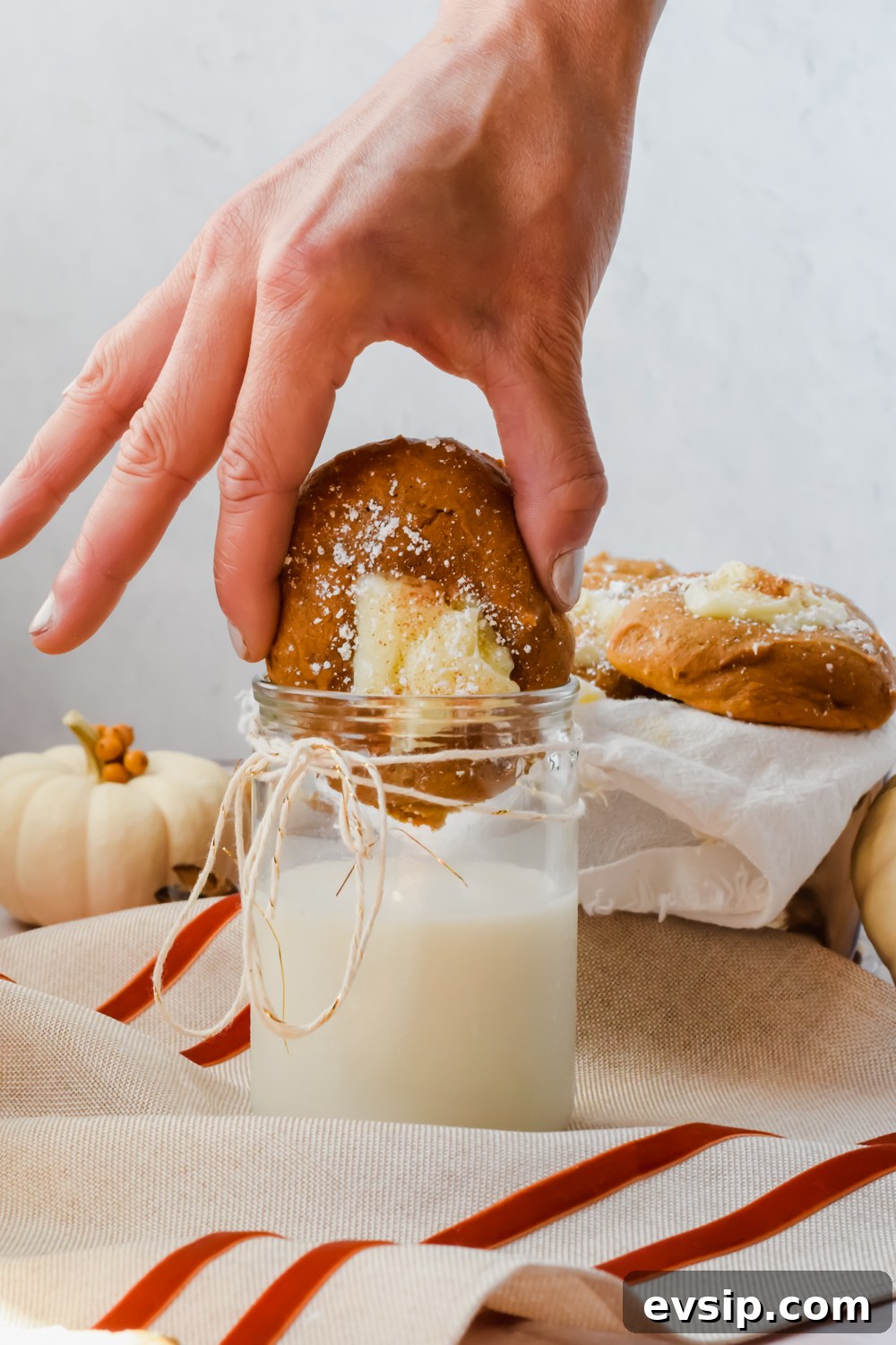 hand dunking pumpkin cheesecake cookie into glass of milk with additional cookies in background.