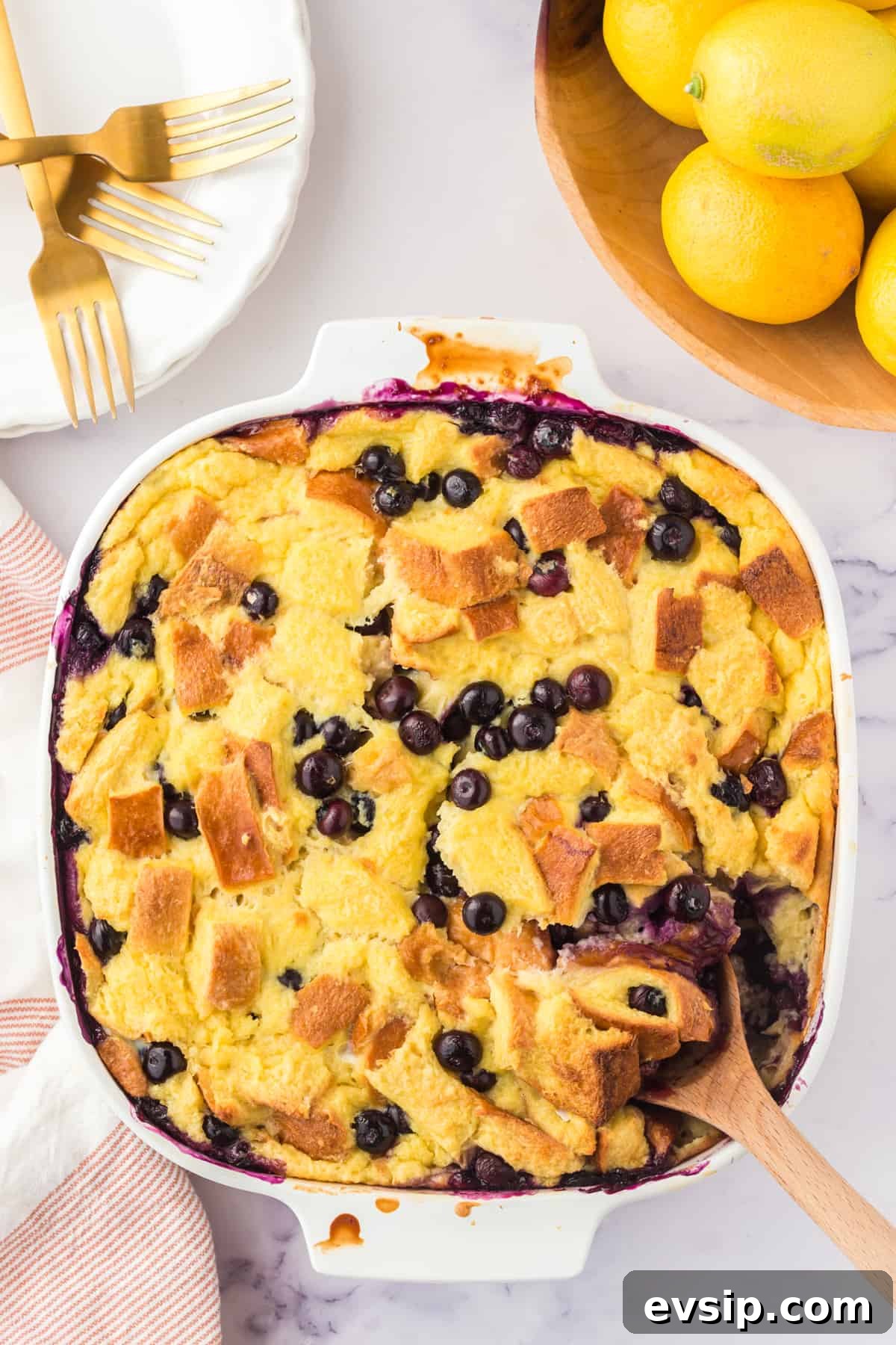 Lemon Blueberry Bread Pudding Recipe 2 Lemon blueberry bread pudding in an square baking dish with wooden spoon sticking out of the corner.