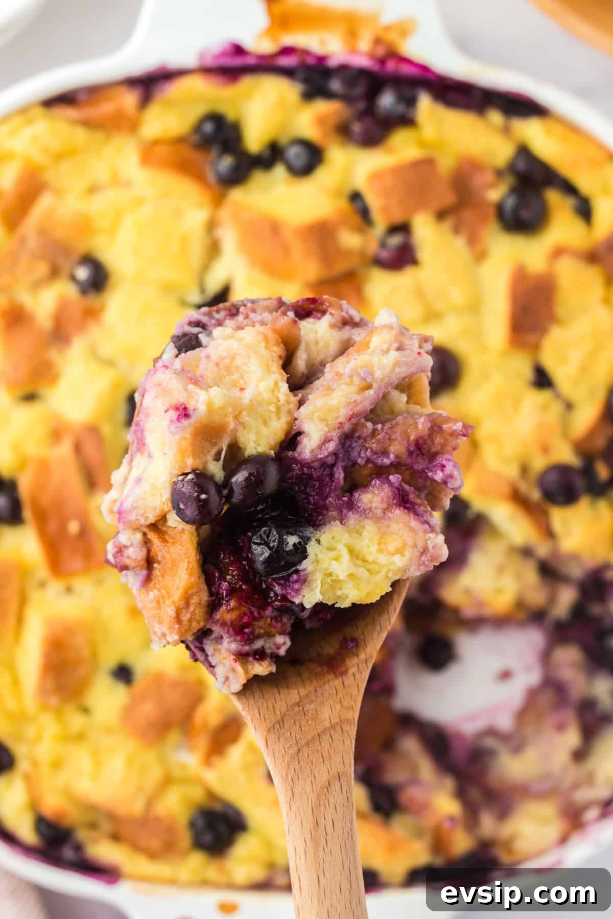 Lemon Blueberry Bread Pudding Recipe 8 Wooden serving spoon lifting a spoonful of bread pudding out of the dish.