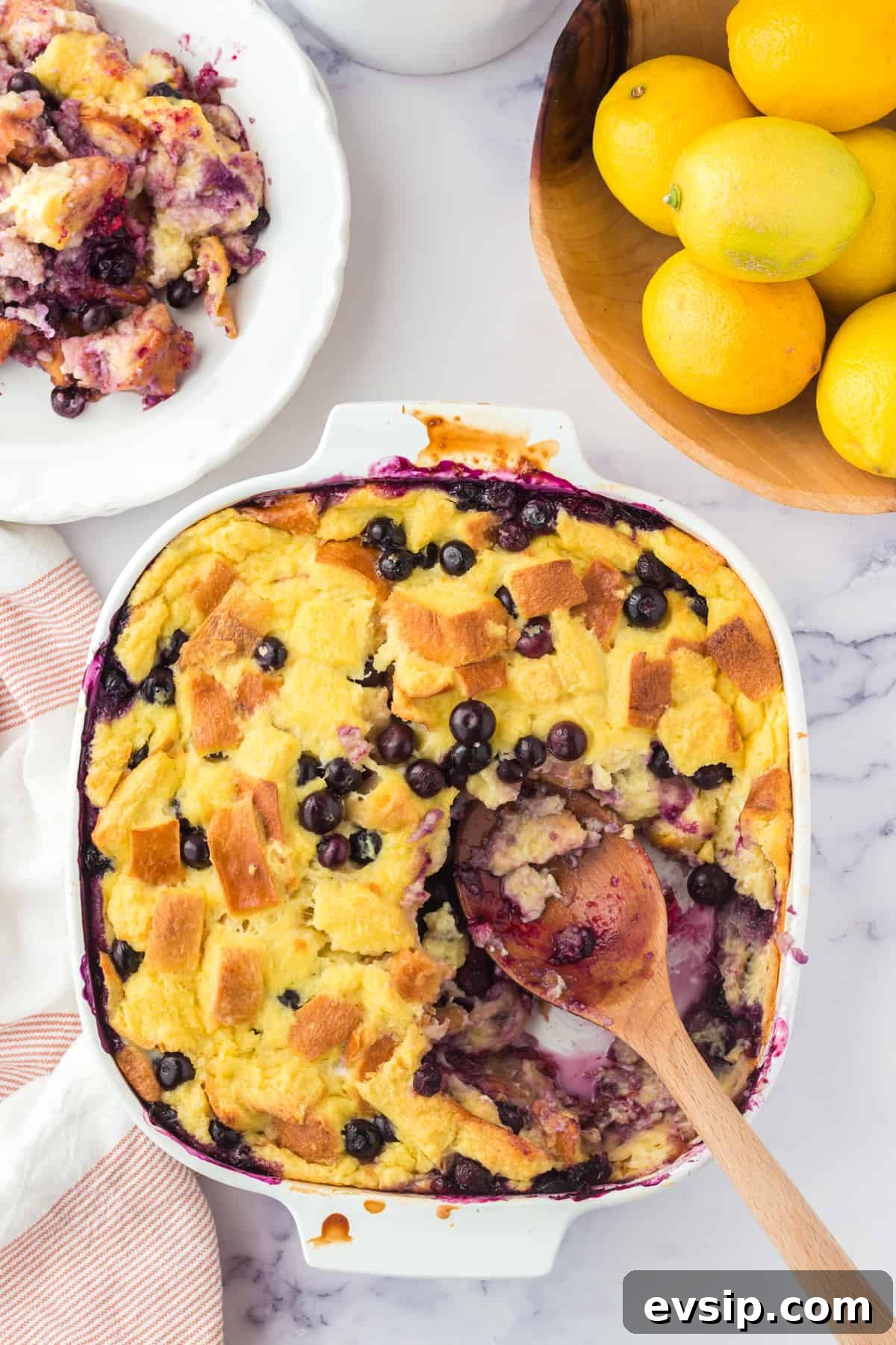 Lemon Blueberry Bread Pudding Recipe 9 Lemon Blueberry Bread pudding with wooden serving spoon resting in dish after several servings were removed.